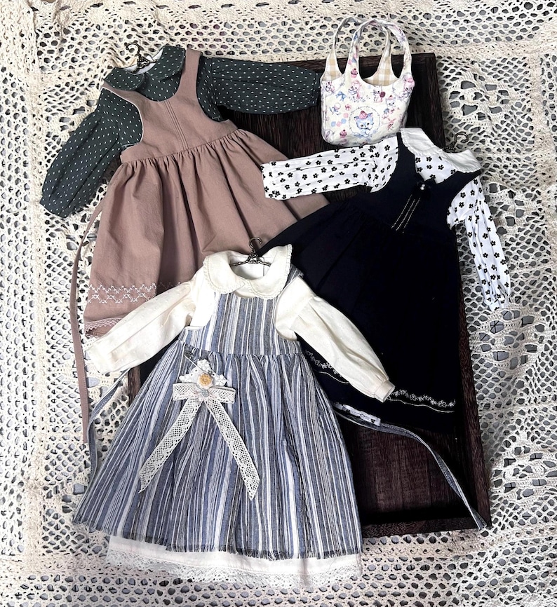 Pode incluir: Tr&ecirc;s vestidos de boneca com blusas combinando. Os vestidos s&atilde;o marrom, preto e listrado azul e branco. As blusas s&atilde;o verdes com bolinhas brancas, pretas com bolinhas brancas e brancas com gola branca.