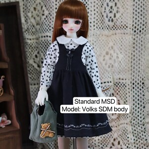 Pode incluir: Uma boneca vestindo um vestido preto e branco com uma gola branca e uma bolsa verde com um urso de pel&uacute;cia. A boneca tem cabelo castanho e olhos verdes. A boneca &eacute; um modelo Standard MSD: Volks SDM body.