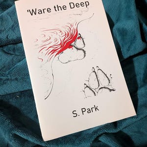 May include: A paperback book titled "'Ware the Deep" by S. Park. The cover features a red and black illustration of a face, paw prints, and abstract shapes on a white background. The book rests on a teal blanket.