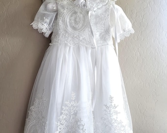 Peut inclure: Robe de baptême en dentelle blanche avec un bonnet assorti. La robe est ornée de broderies délicates et d'un ourlet festonné.