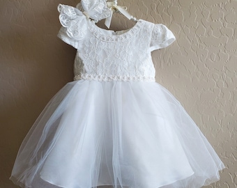 May include: White lace baby dress with a tulle skirt and a matching lace headband. The dress has a round neckline and short sleeves.