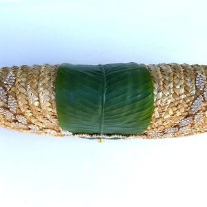 May include: A straw clutch bag with a green leaf design and rhinestones. The bag is woven and has a gold clasp.