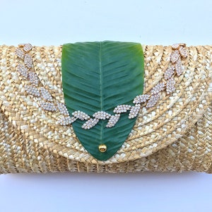 May include: A straw clutch bag with a green leaf design and a rhinestone embellishment.