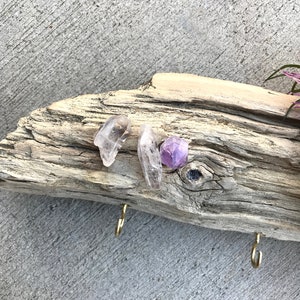 May include: A piece of driftwood with two gold hooks and three crystals: a clear quartz point, a clear quartz cluster, and a purple amethyst.