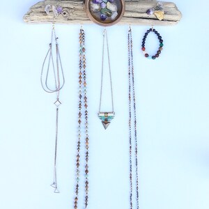 May include: A driftwood jewellery organiser with a small bowl filled with colourful stones. The organiser has hooks for hanging necklaces and bracelets. There are four necklaces and one bracelet hanging from the organiser.