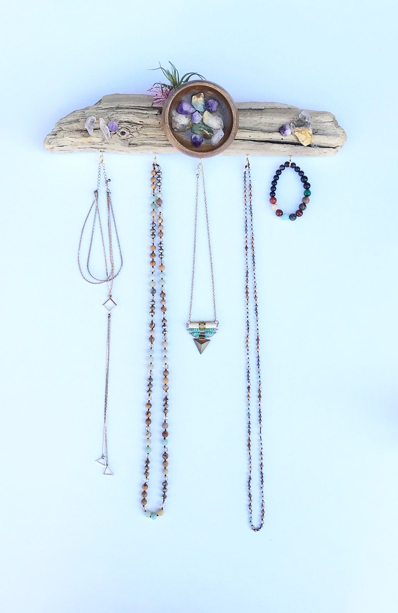 May include: A driftwood jewellery organiser with a small bowl filled with colourful stones. The organiser has hooks for hanging necklaces and bracelets. There are four necklaces and one bracelet hanging from the organiser.
