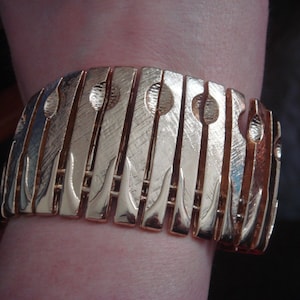 May include: A gold-toned bracelet with a geometric design. The bracelet is made of multiple linked pieces, each with a textured surface.