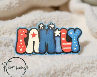 May include: A colorful, layered word art piece spelling "FAMILY". The letters are in red, white, and blue, with star accents. The design has a black outline and a light blue border. The Farmhouse Goodies logo is in the lower left corner.