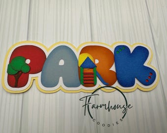 May include: A die-cut paper sign spelling the word PARK in large, colorful, bubble-style letters. The P is red with a green tree, the A is light blue, the R features a yellow sun and a playground slide, and the K is dark blue with dots.