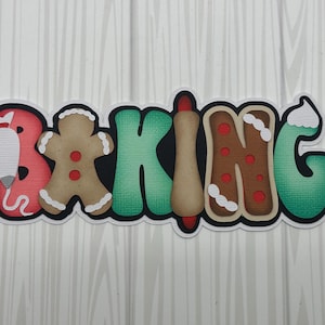 May include: A colorful word art piece that says "BAKING" with each letter decorated with a different baking theme. The "B" is a red rolling pin, the "A" is a gingerbread man, the "K" is green, the "I" is a brown rolling pin, the "N" is a gingerbread cookie, and the "G" is green.