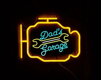Peut inclure: Enseigne au néon jaune en forme de moteur de voiture avec le texte "Dad's Garage" en lettres néon bleues et un graphique de clé.
