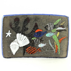 May include: A ceramic tile with a blue border and a gray background depicting a seascape with white, black, blue, red, orange, green, and yellow fish, seaweed, and a seashell.