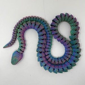 May include: An iridescent green, purple and blue snake sculpture made of plastic. The snake is curled into a figure of eight shape.