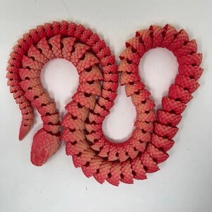May include: A red and orange plastic snake toy with a segmented body. The snake is curled into a figure of eight shape.