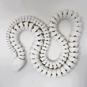 May include: White ceramic snake sculpture with a segmented body. The snake is curled into a figure of eight shape.