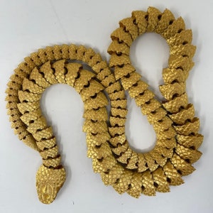 May include: A gold-coloured snake sculpture made of interlocking scales. The snake is curled into a figure of eight shape.