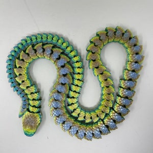Peut inclure: Une sculpture en forme de serpent de couleur verte, bleue et dorée, en céramique ou en plastique. La sculpture est composée de nombreuses petites écailles qui se chevauchent.