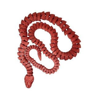 Peut inclure: Un jouet serpent articulé rouge avec un aspect texturé et écailleux. Le serpent est enroulé et courbé, avec une tête détaillée et un corps segmenté. Le jouet est fait d'un matériau brillant et métallique.