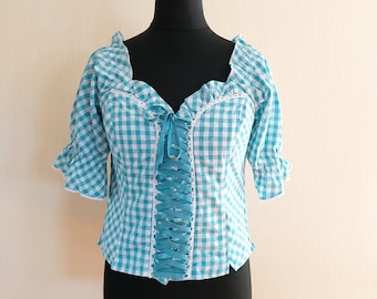 Puede incluir: Una blusa de cuadros azules y blancos con ribete de encaje y un lazo azul en la parte delantera.