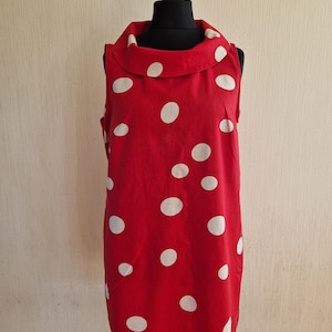 Könnte beinhalten: Rotes ärmelloses Kleid mit weißen Polka Dots. Das Kleid hat einen breiten, runden Kragen und wird auf einer Schaufensterpuppe präsentiert. Der Stoff scheint Baumwolle mittleren Gewichts oder ein ähnliches Material zu sein. Das Kleid ist etwa 90 cm lang.