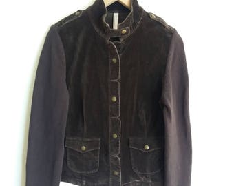 Op de afbeelding: Een bruin corduroy jack met gebreide mouwen en gouden knopen. Het jack heeft twee klepzakken aan de voorkant.