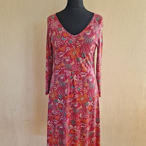 May include: A long-sleeved, V-neck dress with a vibrant floral pattern in shades of red, orange, and pink. The dress features a fitted bodice and a flowing skirt, displayed on a mannequin. The fabric has a soft, textured appearance.