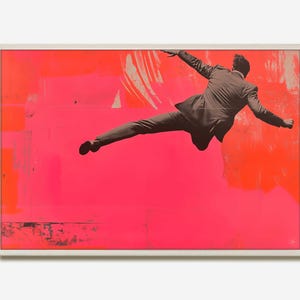 May include: Framed art print showing a man in a suit mid-air against a bright pink and orange abstract background. The artwork is in a white frame, with the text "DEIDHREWAUCHOPSTUDIO" printed vertically on the left side.