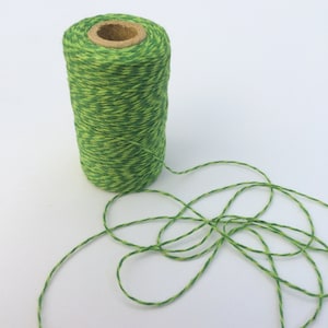 May include: A spool of green and yellow twine with a wooden centre. The twine is unwound and lying on a white surface.