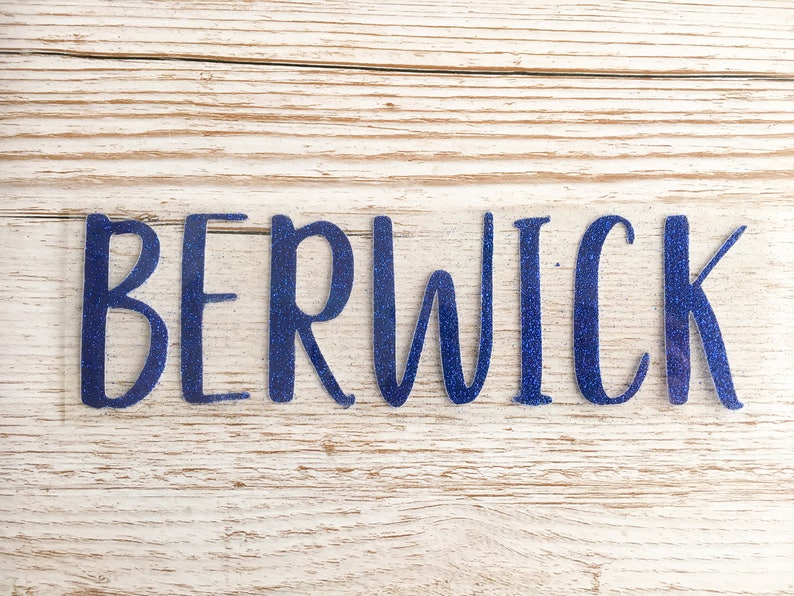 May include: Blue glitter vinyl lettering spelling out the word "BERWICK" on a light wood background.