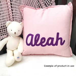 May include: A pink pillow with the name "Alease" embroidered in purple glitter. The pillow is shown with a white teddy bear.