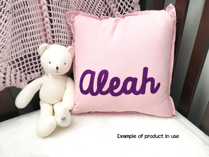 May include: A pink pillow with the name "Alease" embroidered in purple glitter. The pillow is shown with a white teddy bear.