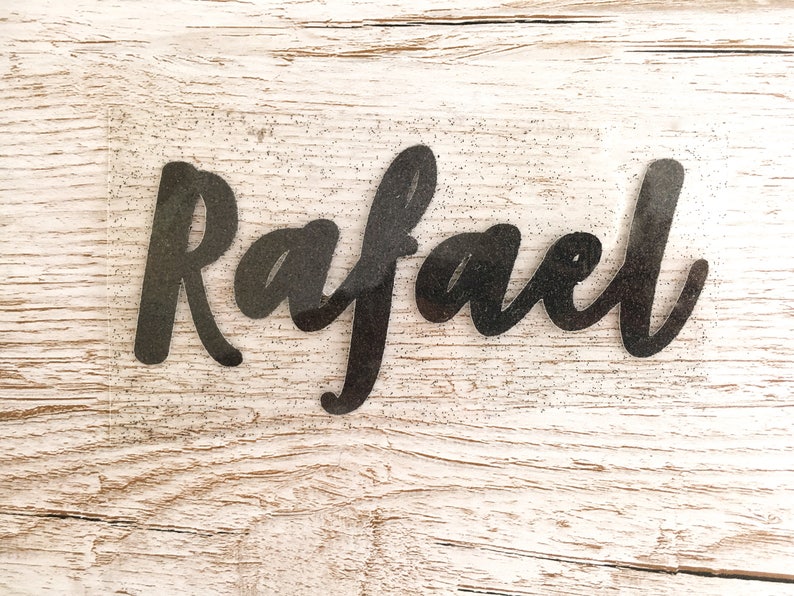 May include: A black glitter vinyl decal with the name "Rafael" written in a cursive font.