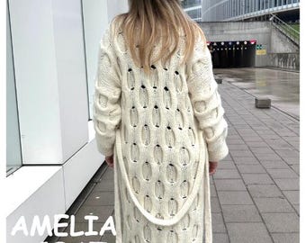 May include: A white knitted cardigan with a cable knit pattern and a long, open front. The cardigan has a belt that can be tied at the waist.