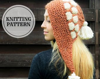 Puede incluir: Un gorro de punto con una solapa larga y puntiaguda en la parte posterior. El gorro es naranja con diseños geométricos blancos y pompones blancos.