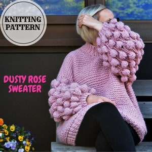 Könnte beinhalten: Staubiger rosafarbener Strickpullover mit großen, bauschigen Ärmeln. Der Pullover hat eine lockere Passform und einen hohen Kragen.