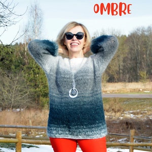 May include: A woman wearing a gray, blue, and white ombre sweater with a silver necklace and red pants. The word "OMBRE" is written in red letters at the top of the image.