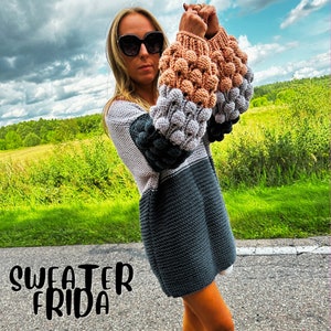 May include: A gray, black, and beige knitted sweater with large, puffy sleeves. The sweater has a loose fit and a slightly cropped length.
