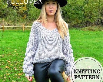 May include: A grey knitted pullover with a v-neck and large, puffy sleeves. The sweater is worn by a person wearing a black hat and black leather pants. The text "GREY FOG PULLOVER" is visible at the top of the image. The text "KNITTING PATTERN" is visible in a circle at the bottom right of the image.