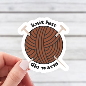 May include: A white sticker with a brown yarn ball and two knitting needles crossed over the ball. The text "knit fast die warm" is written around the yarn ball.