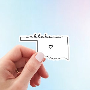 May include: A white sticker with a black outline of the state of Oklahoma and the word "Oklahoma" written above it. A small black heart is inside the outline of the state.