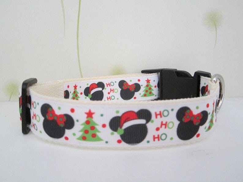 May include: White dog collar with a festive Christmas design. The collar features black Mickey Mouse silhouettes with red bows and Santa hats, green Christmas trees, and the words "HO HO HO" in red and green.