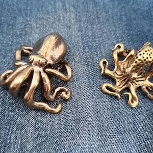 May include: Two gold-colored octopus figurines. The octopus on the left has a smooth surface, while the octopus on the right has a textured surface.