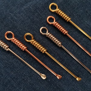 May include: Six metal tools with a coiled handle and a rounded tip. The tools are silver, gold, and copper.