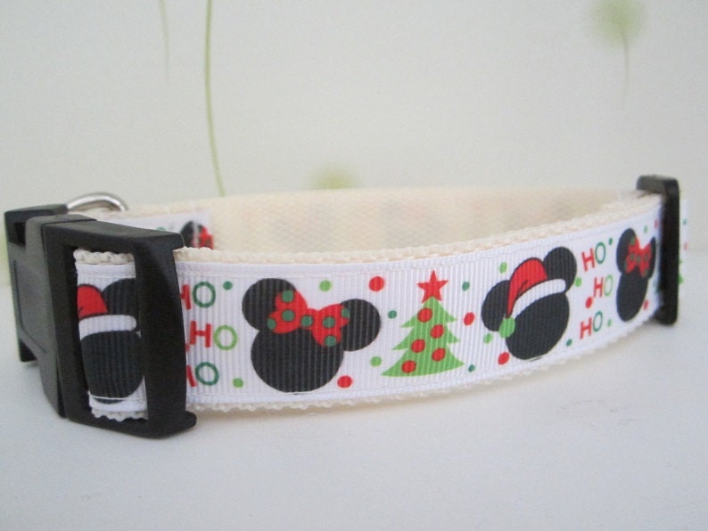May include: White dog collar with a black plastic buckle. The collar features a repeating pattern of black mouse silhouettes with red bows and Santa hats, green Christmas trees, and the words "HO HO" in green and red.