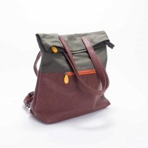 May include: A brown and green canvas and leather backpack with a fold-over top and two adjustable straps. The bag has a zippered pocket on the front and a small orange zipper detail.