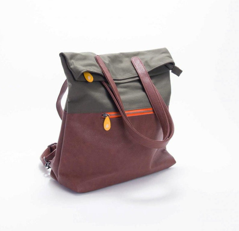 May include: A brown and green canvas and leather backpack with a fold-over top and two adjustable straps. The bag has a zippered pocket on the front and a small orange zipper detail.