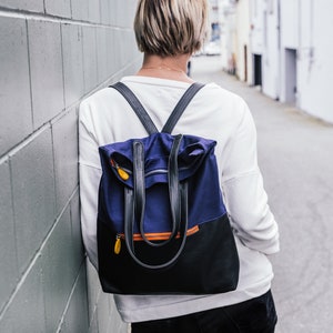 May include: A person wearing a white shirt and black jeans with a blue and black backpack with orange accents.