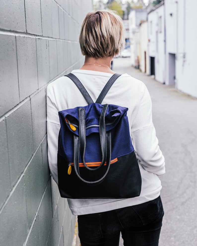 May include: A person wearing a white shirt and black jeans with a blue and black backpack with orange accents.