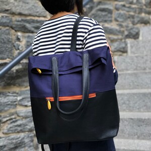 May include: A navy blue and black backpack with a zipper and orange accents. The backpack has a top flap and two adjustable straps.