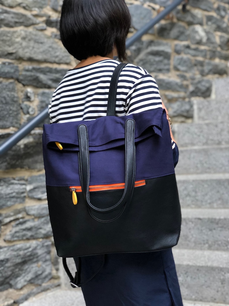 May include: A navy blue and black backpack with a zipper and orange accents. The backpack has a top flap and two adjustable straps.